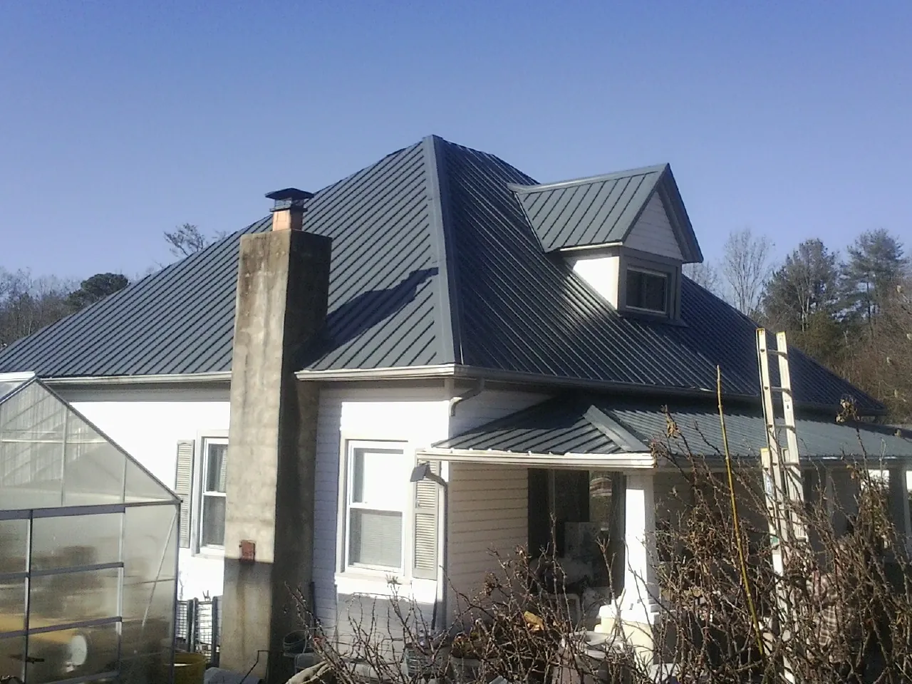 Dark blue standing seam metal roof on a white farmhouse with dormer — Slate & Tile Roof Repair by Roofing Brothers in Burke