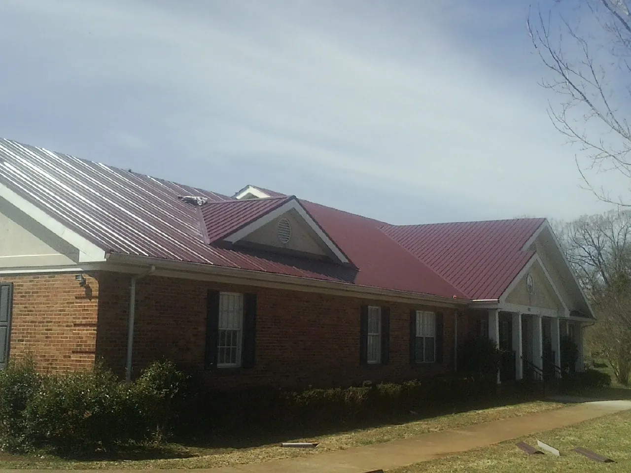 Red metal roof with gabled entries on a long brick building, from a Hail Damage Roof Repair job in Burke