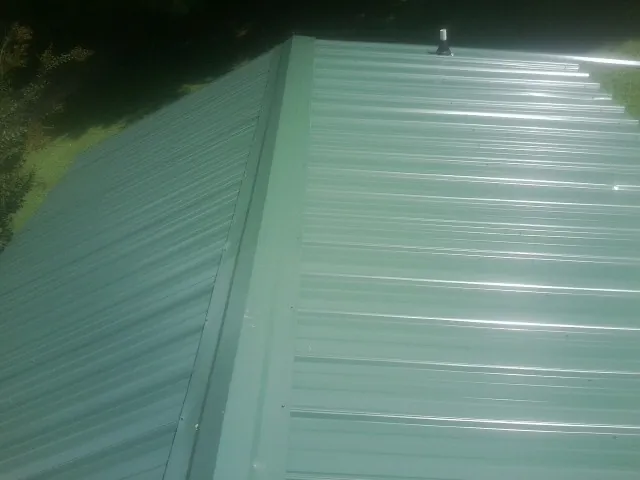 New green metal panels meeting at the ridge of a roof — Flat Roof Repair work by our crew in Burke