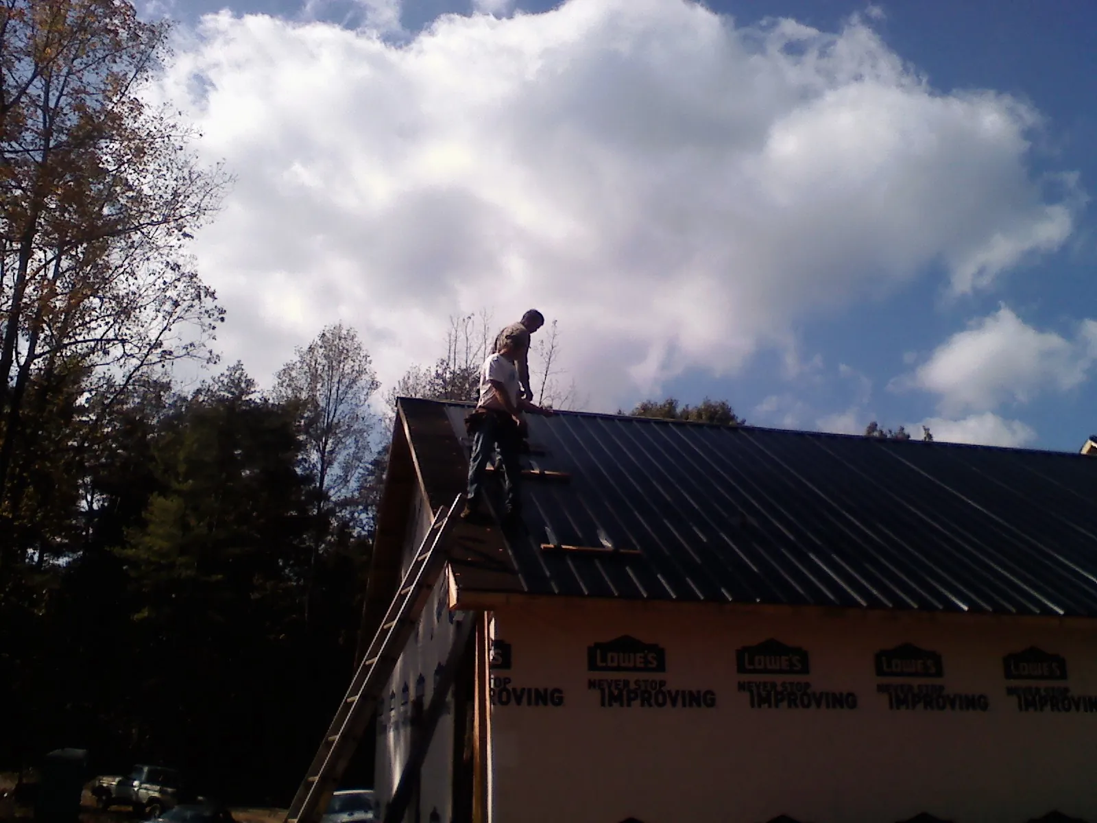 Roofer fastening dark metal panels high against a cloudy sky, from a Roof Inspection job in Burke
