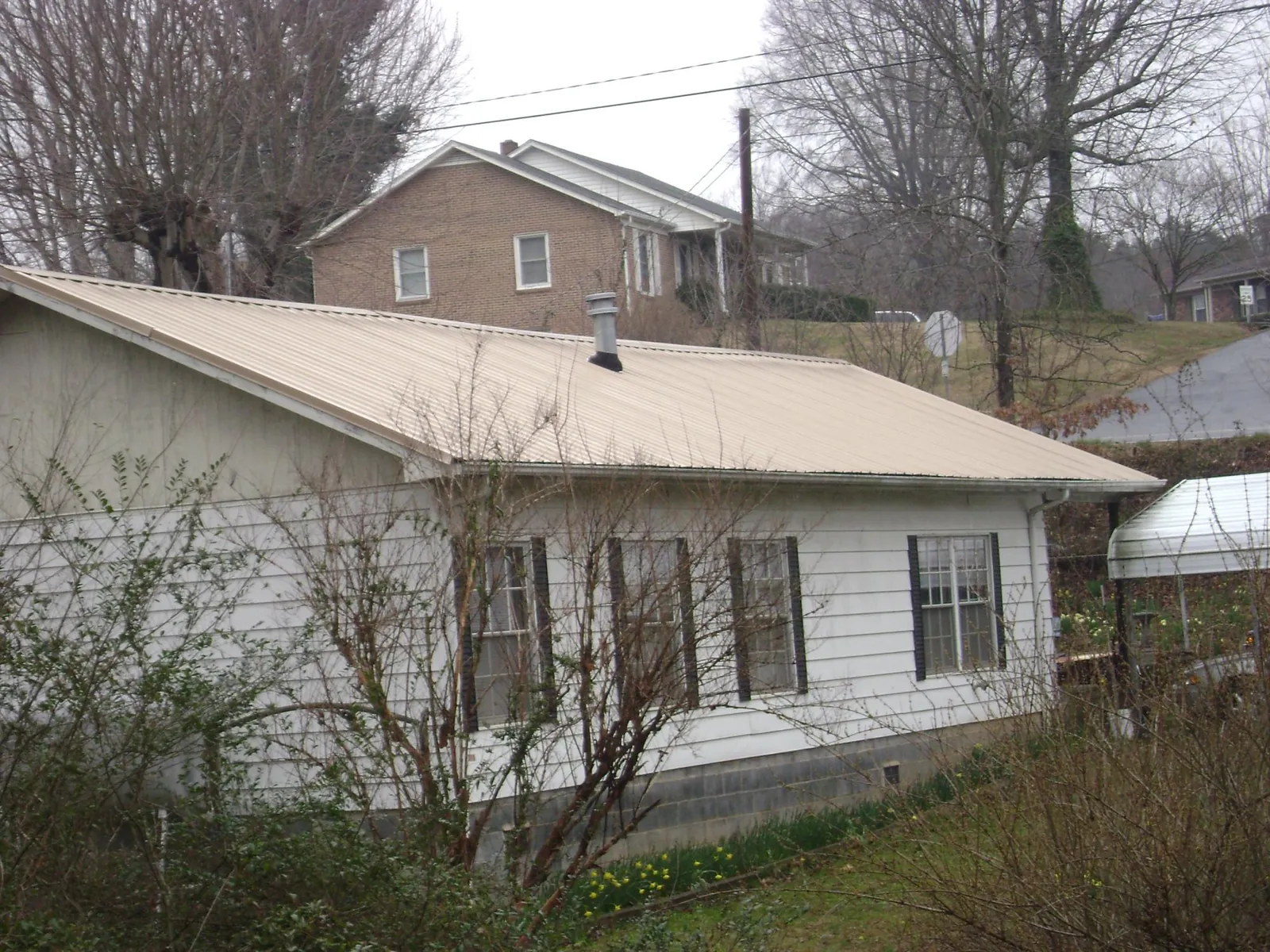 Tan metal roof on a white sided house set into a hillside — Commercial Roofing by Roofing Brothers in Burke